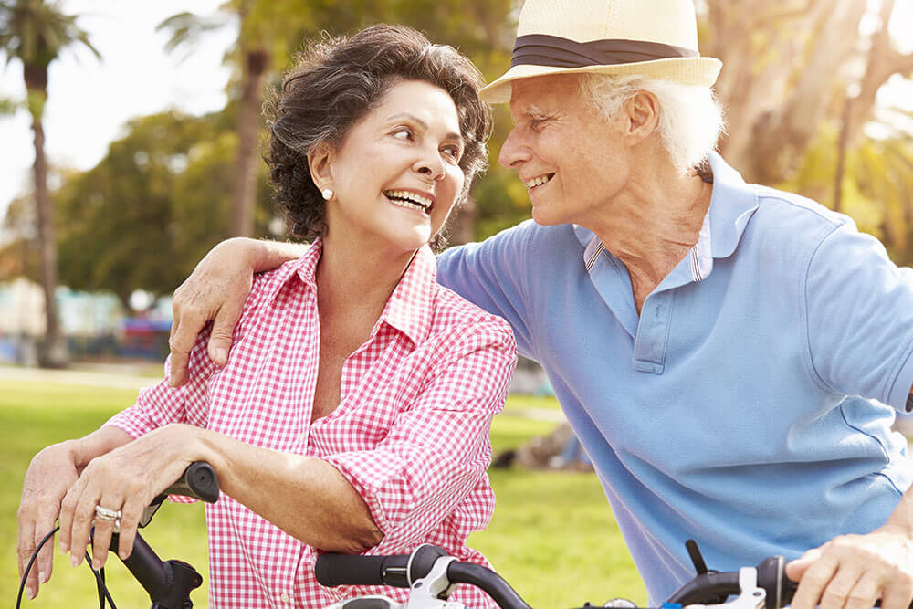 Older man and woman outside in tropical climate. Man has arm around woman's shoulder.