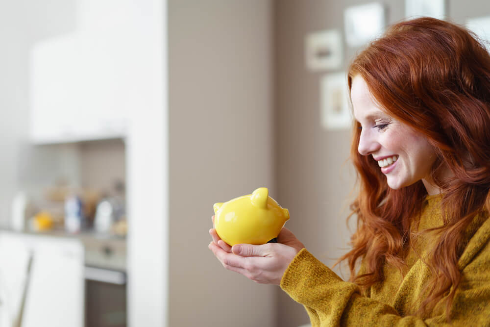 Woman with red hair looking at yellow piggy bank